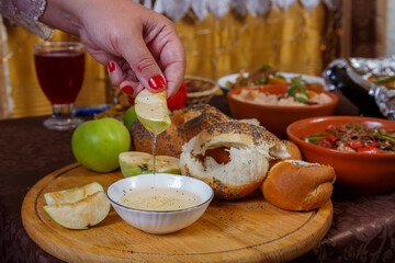 A woman's hand dips an apple in honey at the table on the Jewish holiday Rosh Hashanah.