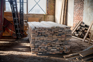 Side view of stack ow wooden pine tree planks lying on floor in sawmill building next to brick wall and window. Soft focus. Lumber industry theme.