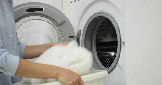 A capable woman takes charge of her chores, loading a pile of grimy garments into the washing machine. Her focused demeanor reflects her determination to maintain a tidy home environment.