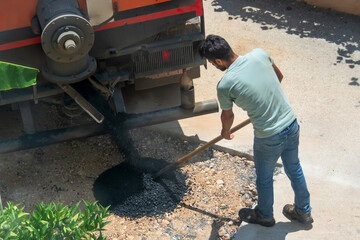 Worker pours and levels fresh asphalt from a truck to be laid onto the street road surface.