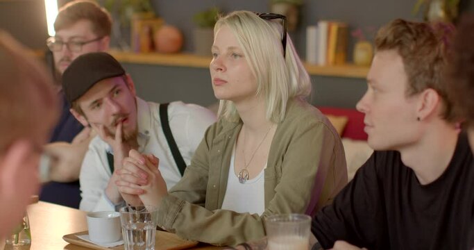 Young woman appears detached and lost in her thoughts during a group conversation, preoccupied own pressing concerns and issues, which occupy mind even as physically present amidst a social gathering.