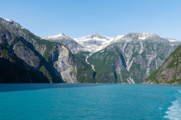 Obraz premium Beautiful landscape of Alaskan mountains at the seashore. The image shows a waterfall falling from the top of the mountain to the blue sea, as a result of snow melting.