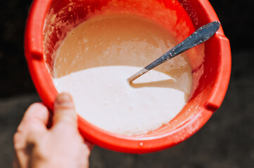 A woman, a cook, holds in her hands a red plastic bowl with batter, dough for baking. Close-up photo of food.