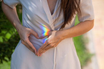 Faceless woman catching rainbow ray with her hands outdoors. Girl makes a heart with her hands