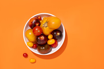 Colorful yellow, red, black tomatoes in a white plate on orange background, top view
