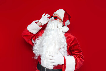 santa claus in glasses touches his mustache on colored background, man in hat and santa costume for christmas