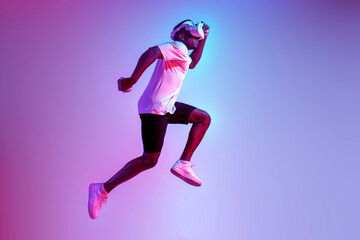 african american athletic man jumping in virtual reality glasses in neon lighting, the guy athlete...