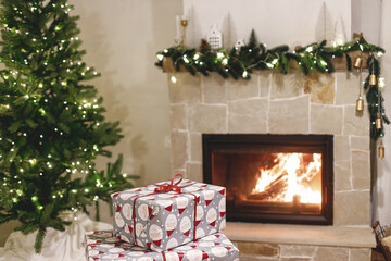 Stylish wrapped christmas gifts, christmas tree with festive lights and cozy burning fireplace. Atmospheric Christmas eve, holiday time. Merry Christmas!