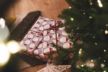 Merry Christmas! Stylish wrapped christmas gifts against christmas tree with festive lights. Atmospheric Christmas eve, holiday time.