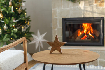 Christmas modern decoration on table against burning fireplace. Stylish wooden star decor in festive room, christmas eve time. Atmospheric christmas time.