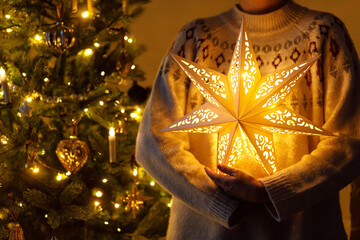 Merry Christmas! Stylish illuminated golden star in hands on background of modern decorated...
