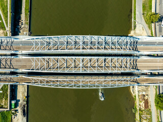 Triple tied-arc railroad bridge with four tracks, footbridge for pedestrians and bicycle lane over Vistula river in Krakow, Poland. Aerial view from above