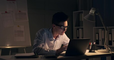 Stressed office worker is seen grappling with a pile of documents. The soft glow of the desk lamp accentuates the late hour and the challenges he faces.
