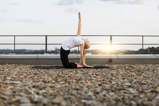Lady exercising back-bend pose while kneeling on gravel roof