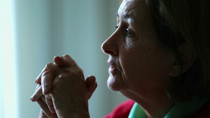 Thoughtful senior woman gazing at window in mental reflection. Pensive elderly lady in contemplation