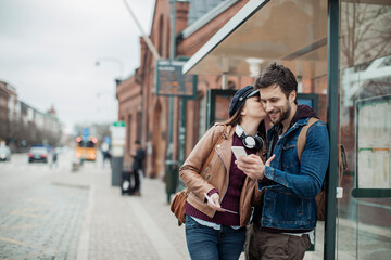 Young couple using a smartphone while waiting for their bus at a bus station