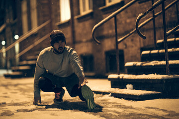 Young man stretching while out jogging and exercising at night during winter and snow in the city