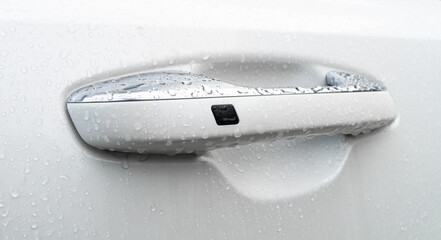 The modern door handle of a white car with water drops. Car exterior details. Closeup Car door handle with keyless system. Car equipment concept.