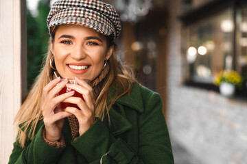 Close up of blonde happy young woman looking at camera while holding cup of tea. Portrait of young beautiful smiling woman holding cup of tea with blurred background.