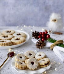 Homemade chocolate hazelnut Christmas cookies presented in a small white dish on a Christmas cloth table with a holly and pine cones decorating a white napkin. 