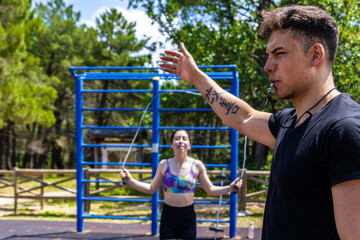 Portrait of a personal trainer with a whistle giving the order to start the exercise while in the background is a girl skipping rope. Physical training