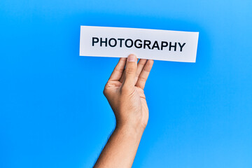 Hand of caucasian man holding paper with photography word over isolated blue background