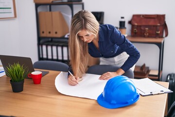 Young blonde woman architect drawing house plans at office