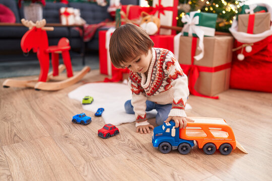 Adorable toddler playing with truck toy sitting on floor by christmas tree at home