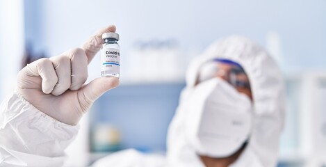 Young hispanic man scientist wearing medical mask holding covid vaccine dose at laboratory