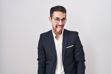 Handsome business hispanic man standing over white background sticking tongue out happy with funny expression. emotion concept.