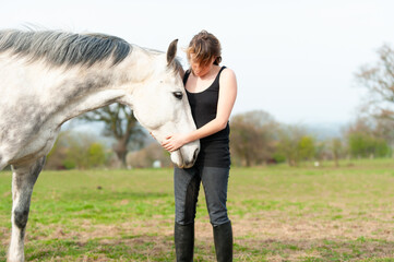 Your head in my hands, pretty young woman stand sharing an emotional moment with her large grey horse in field on a warm summers day.