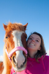 Selfie time, pretty young girl and her chestnut pony horse having a photo taken together in selfie style, smiling happy and with a blue sky backdrop.