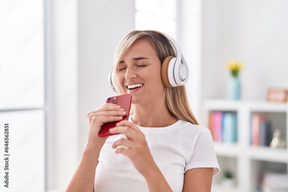 Poster young blonde woman listening to music singing song at bedroom