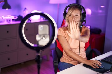 Young blonde woman recording vlog tutorial with smartphone at home with open hand doing stop sign...