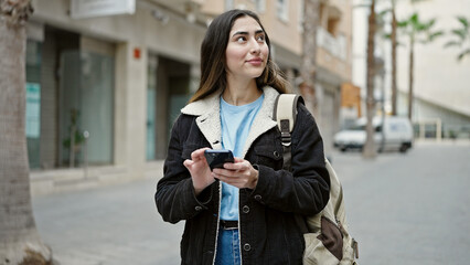 Young beautiful hispanic woman student smiling confident using smartphone at street