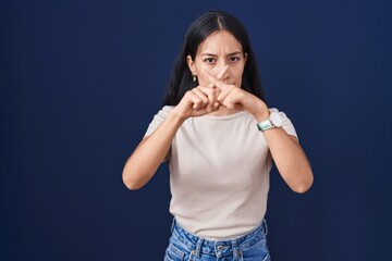 Young hispanic woman standing over blue background rejection expression crossing fingers doing negative sign