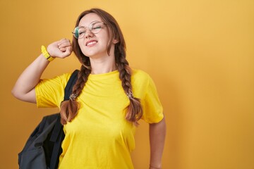 Young caucasian woman wearing student backpack over yellow background stretching back, tired and relaxed, sleepy and yawning for early morning