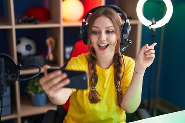 Young caucasian woman playing video games with smartphone smiling happy pointing with hand and finger to the side