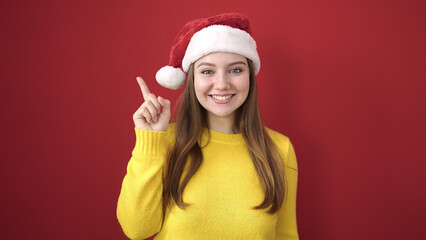 Young blonde woman wearing christmas hat with idea gesture over isolated red background