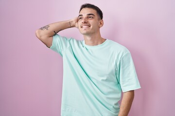 Obraz premium Handsome hispanic man standing over pink background smiling confident touching hair with hand up gesture, posing attractive and fashionable