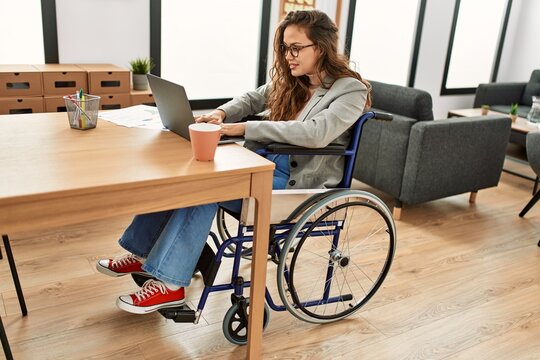 Young beautiful hispanic woman business worker using laptop sitting on wheelchair at office