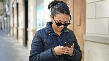 Naklejka premium Young beautiful hispanic woman using smartphone smiling at street