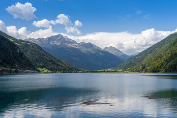 Swiss alpine lake in the mountains, Poschiavo (Miralago), Switzerland. Bernina massif peaks in the background of the green valley, blue sky with clouds.