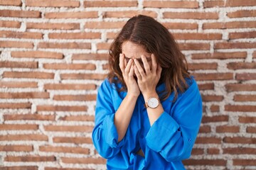 Beautiful brunette woman standing over bricks wall with sad expression covering face with hands while crying. depression concept.