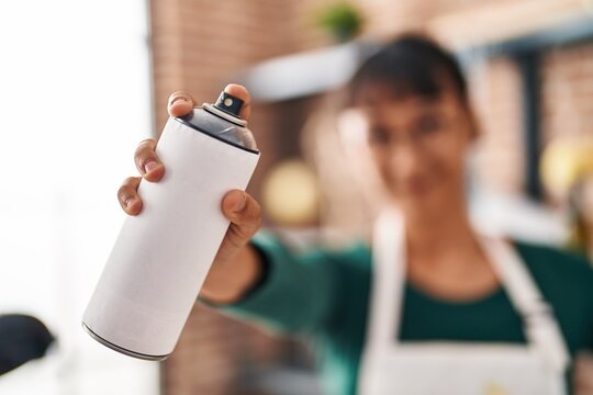 Young beautiful hispanic woman artist smiling confident holding graffiti spray at art studio