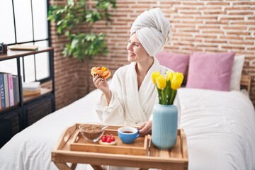 Young blonde woman wearing bathrobe having breakfast at bedroom