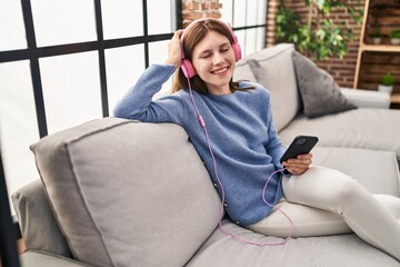 Obraz premium Young blonde woman listening to music sitting on sofa at home