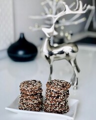 Christmas homemade chocolate and seeded cookies presented in a small square dish to friends with a Christmas silver deer figure decorating the table.