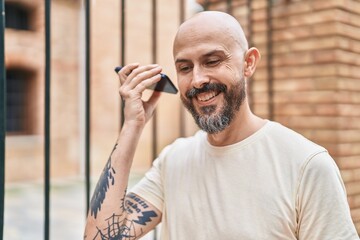 Young bald man smiling confident listening audio message by the smartphone at street
