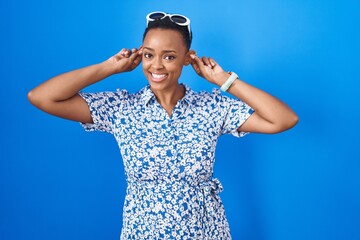 African american woman standing over blue background smiling pulling ears with fingers, funny...